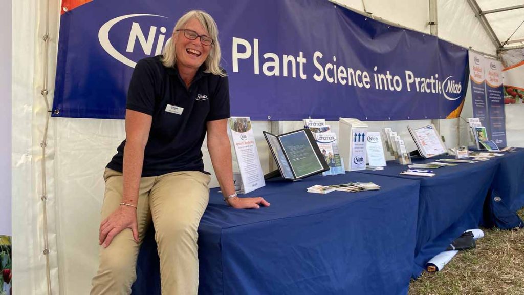 Researcher, Clare Leaman sits on the display table at the Morley Innovation Day, smiling to the camera